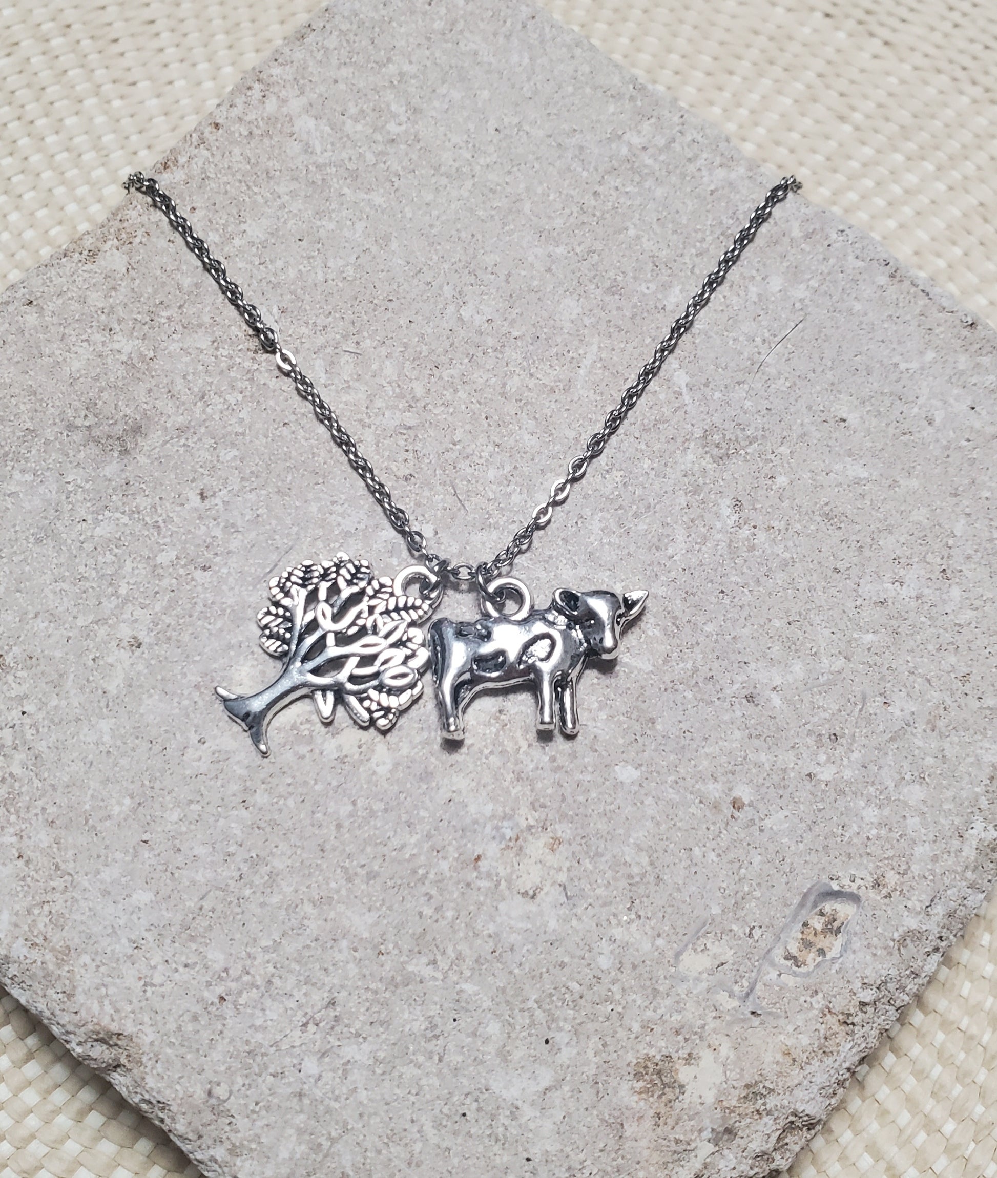 An INTO THE WOODS Milky White Necklace by The Lobby Boutique with a bull charm and a tree charm.