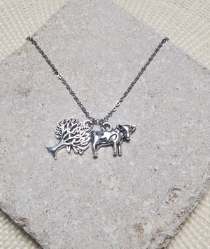 An INTO THE WOODS Milky White Necklace by The Lobby Boutique with a bull charm and a tree charm. An INTO THE WOODS Milky White Necklace by The Lobby Boutique with a bull charm and a tree charm.