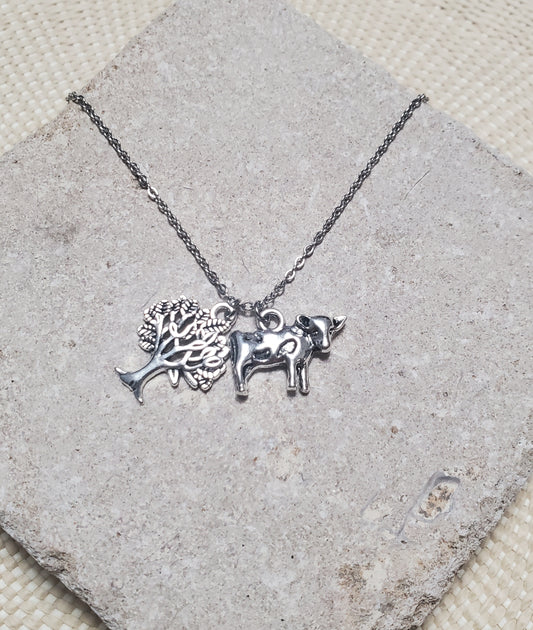 An INTO THE WOODS Milky White Necklace by The Lobby Boutique with a bull charm and a tree charm.