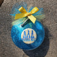 A MAMMA MIA Christmas Ornament by The Lobby Boutique featuring a blue glass design and a yellow ribbon.