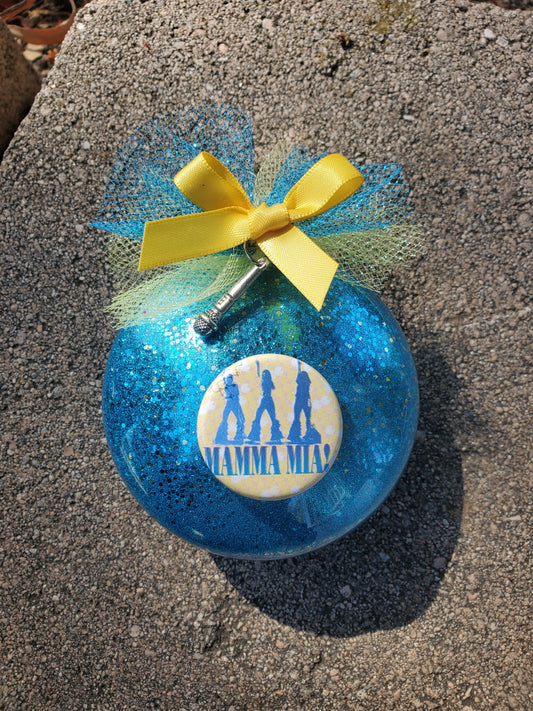 A MAMMA MIA Christmas Ornament by The Lobby Boutique featuring a blue glass design and a yellow ribbon.