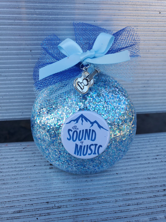 A blue glitter SOUND OF MUSIC Christmas Ornament with the words "Sound of Music" for theatre merchandise from The Lobby Boutique.
