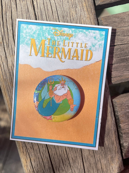a metal pinback button with a graphic of King Triton from the Little Mermaid from the Lobby Boutique on Etsy